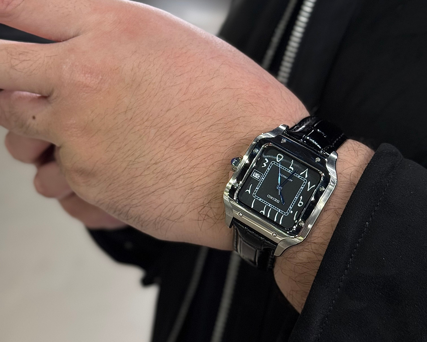 Hand wearing a black and silver watch with a blurred background