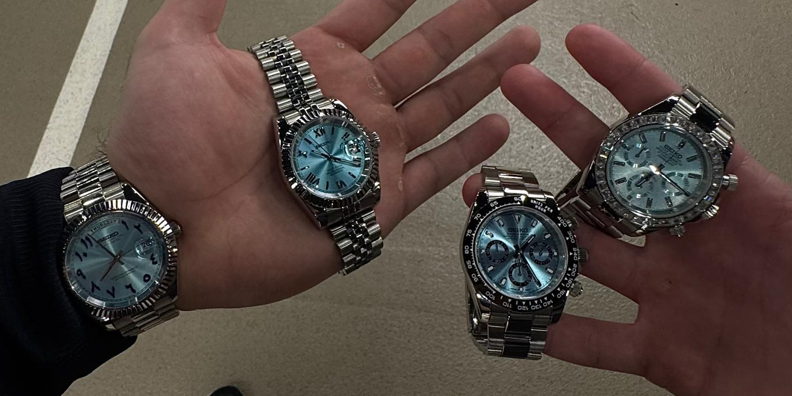 Two hands wearing silver watches with blue faces on a beige background